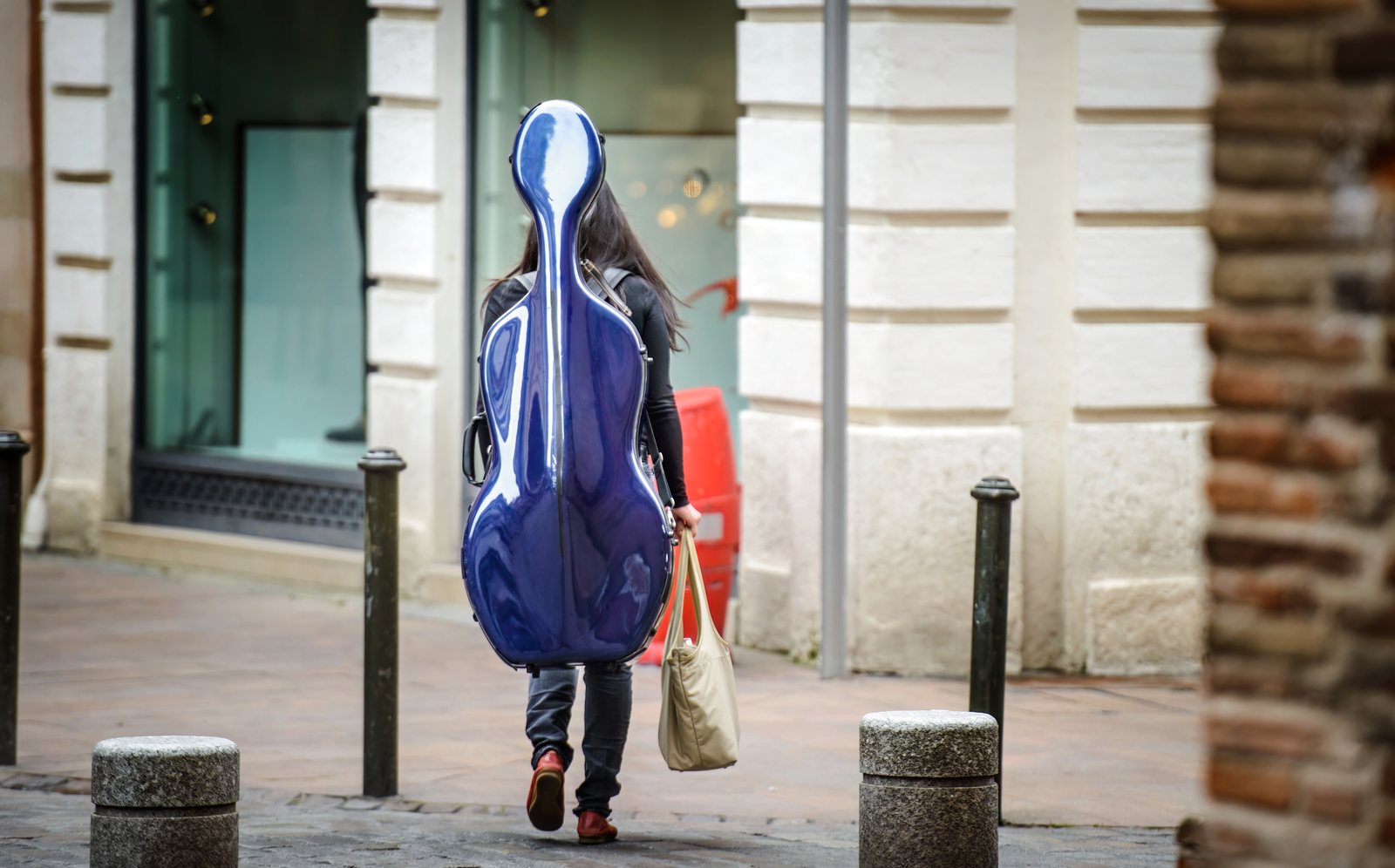 Cellistin trägt einen blauen Cellokasten im Stadtraum